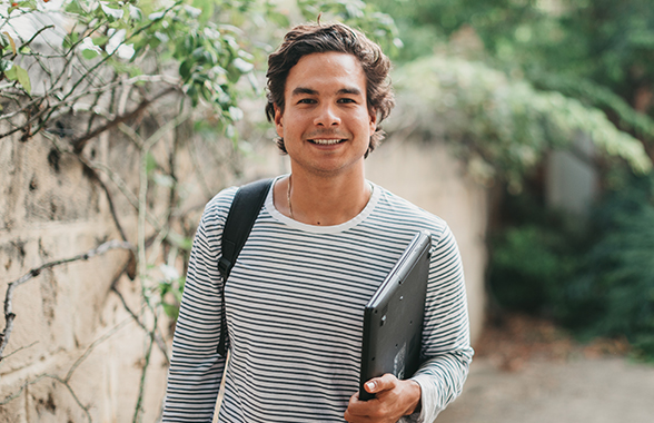 UWA Student carrying laptop and backpack in front of wall